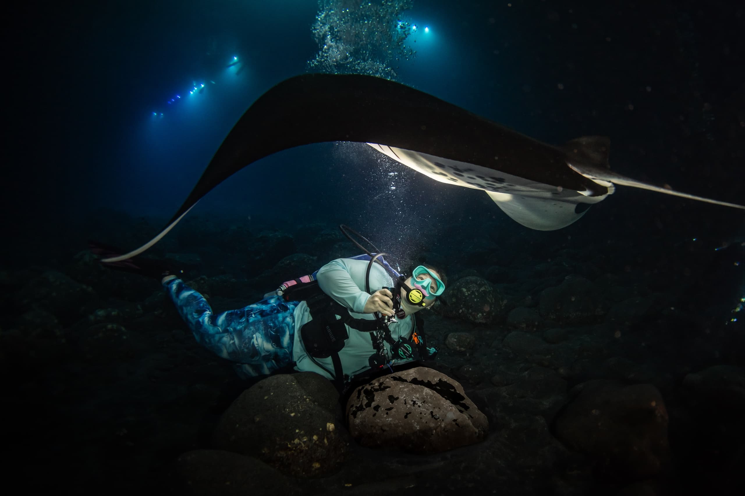Night manta ray encounter with diver photographing on reef