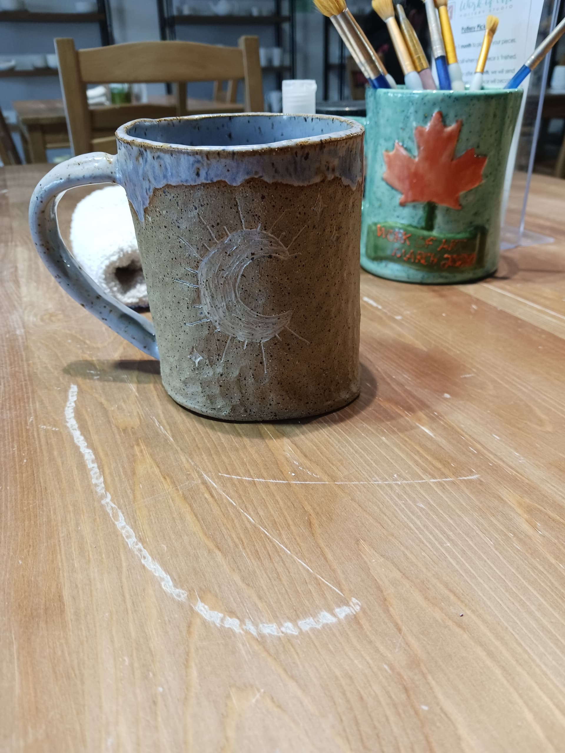 Handmade ceramic mug and brushes on wooden studio table
