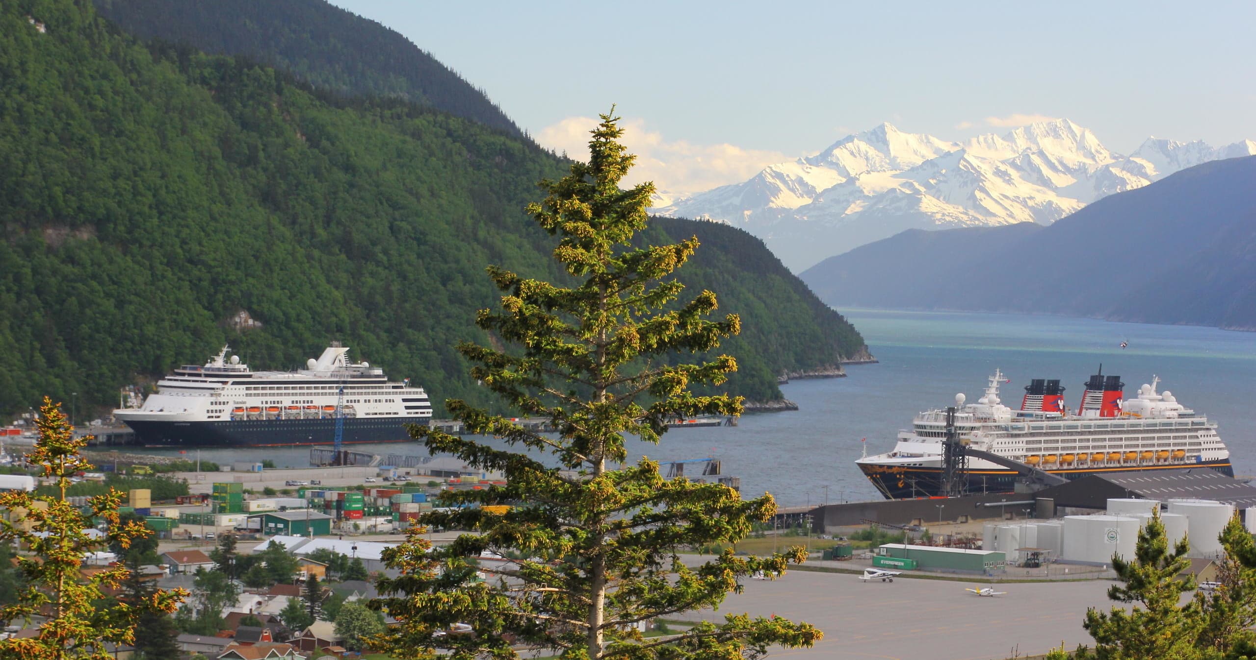 Cruise ships docked in mountain fjord harbor with snow peaks
