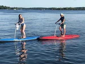 Two people riding electric stand-up paddleboards on calm lake
