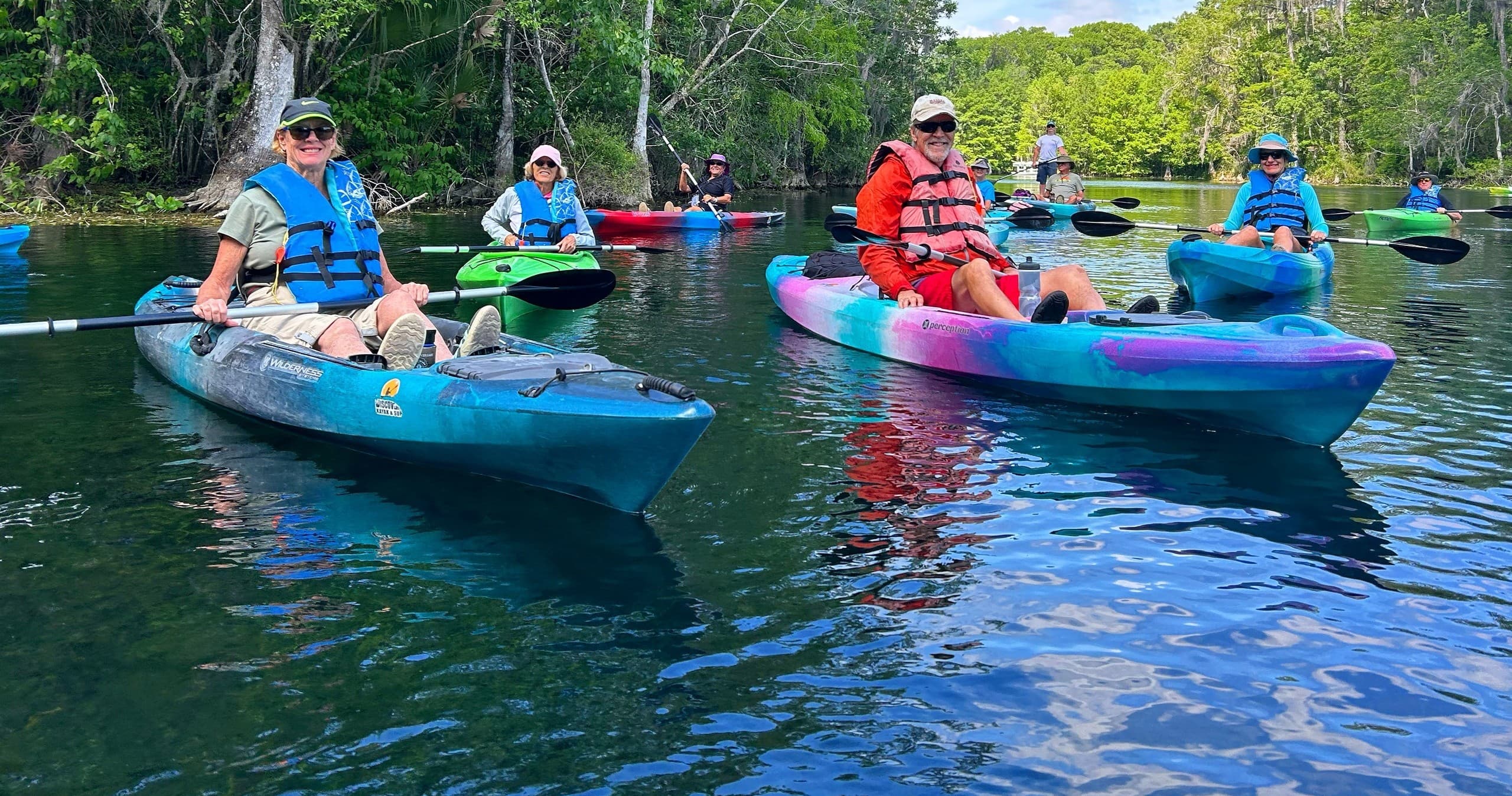 Close-up kayakers on emerald water near river trees