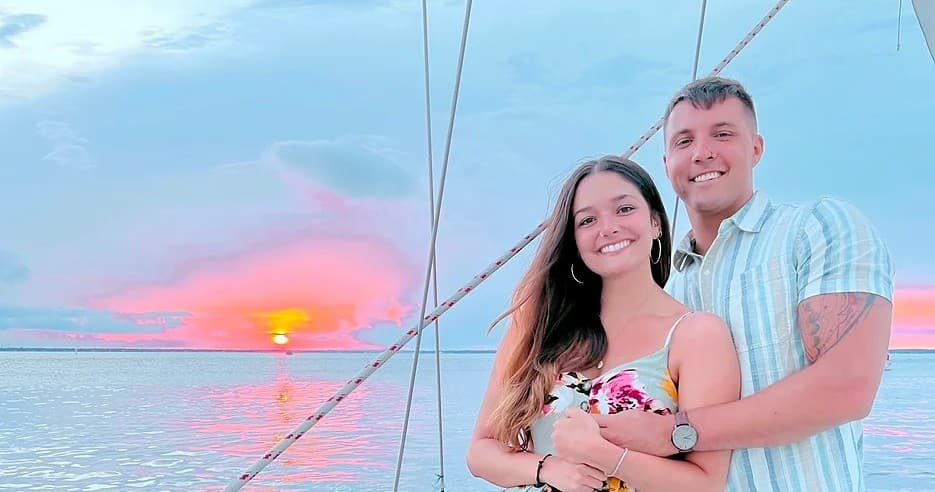 Couple sailing at sunset on open ocean aboard sailboat