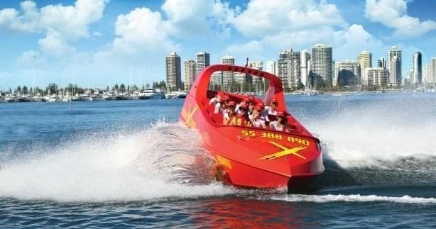 Red jet boat racing past urban skyline on sunny ocean waters