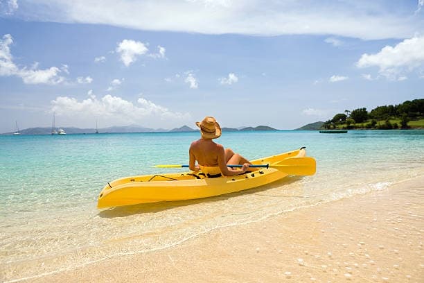 Solo kayaker relaxing on yellow kayak at tropical sandy beach