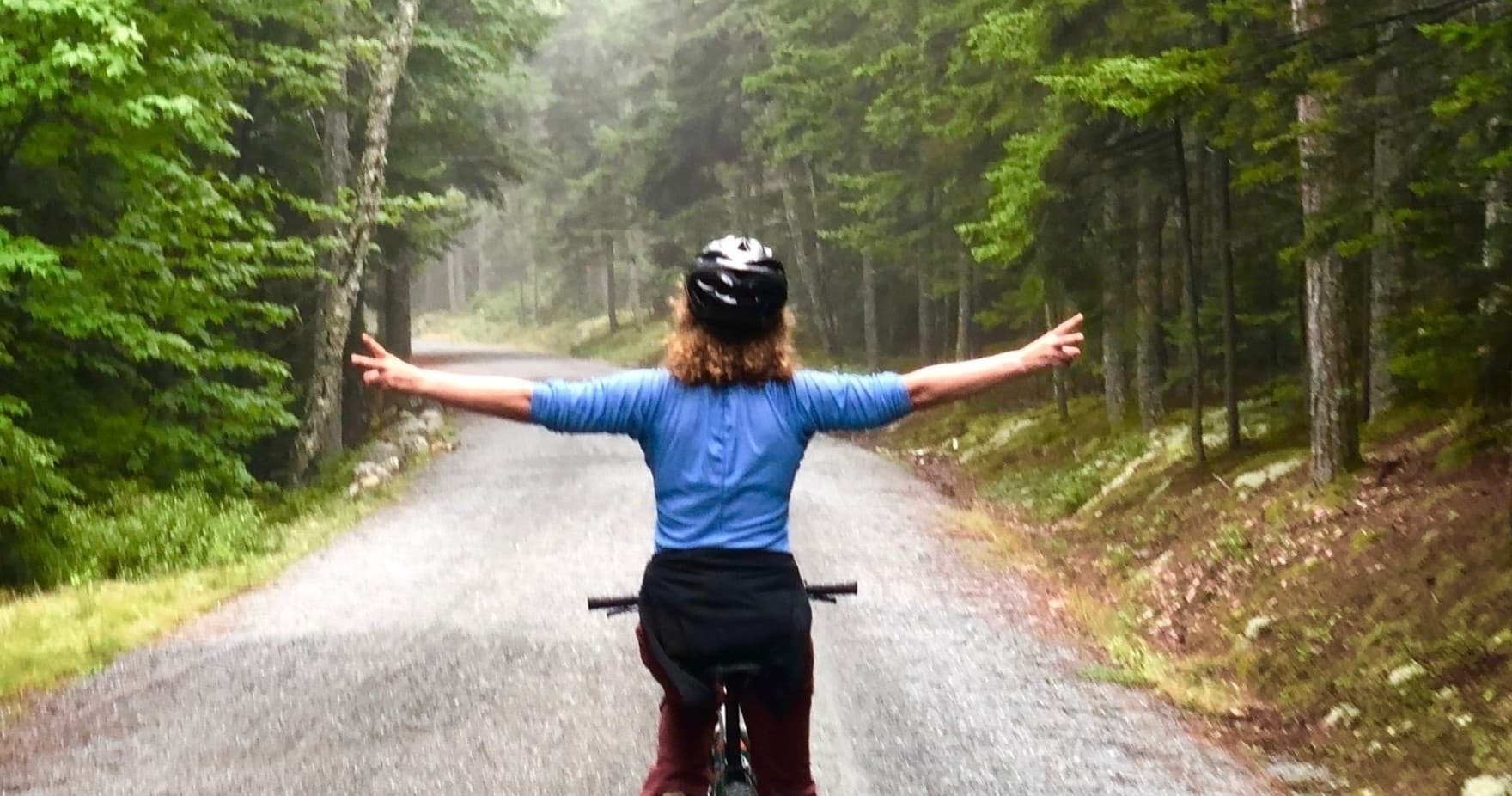 Cyclist riding forest road with arms outstretched on trail