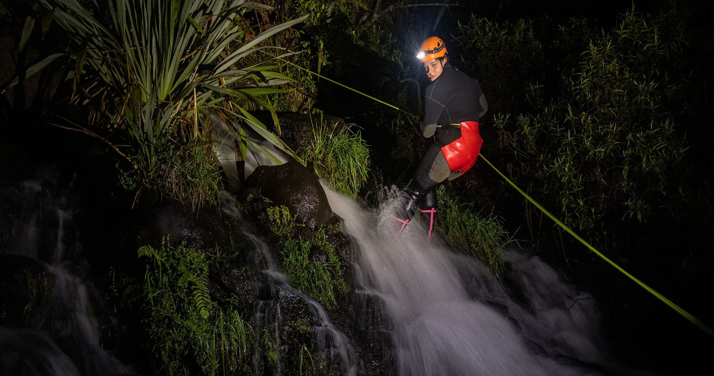 Rappelling down a waterfall at night through forested canyon