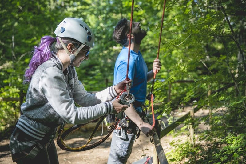 Staff guiding climber on zipline harness at forest adventure park