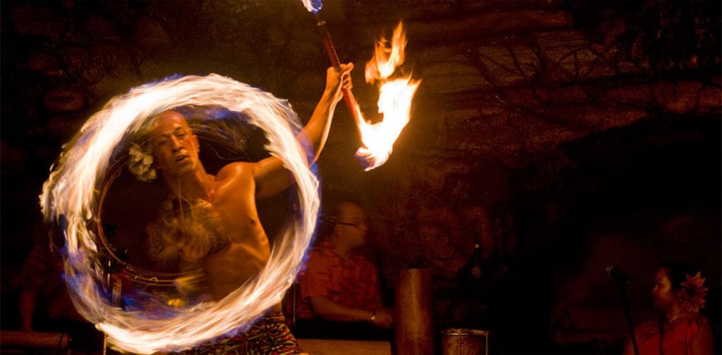 Fire dancer performing torch routine at nighttime luau show