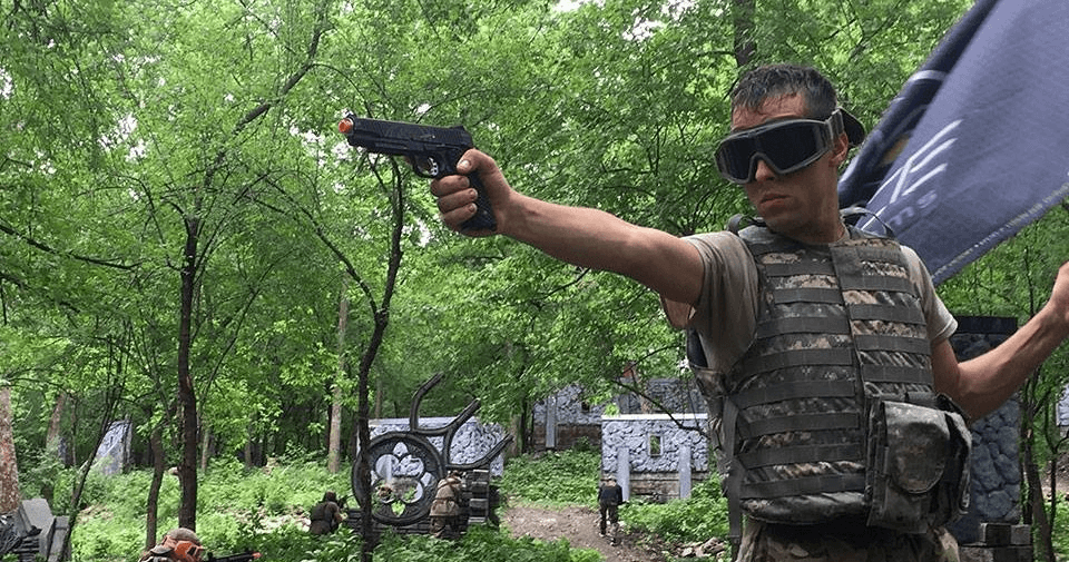 Participant aiming pistol in wooded tactical airsoft scenario at park