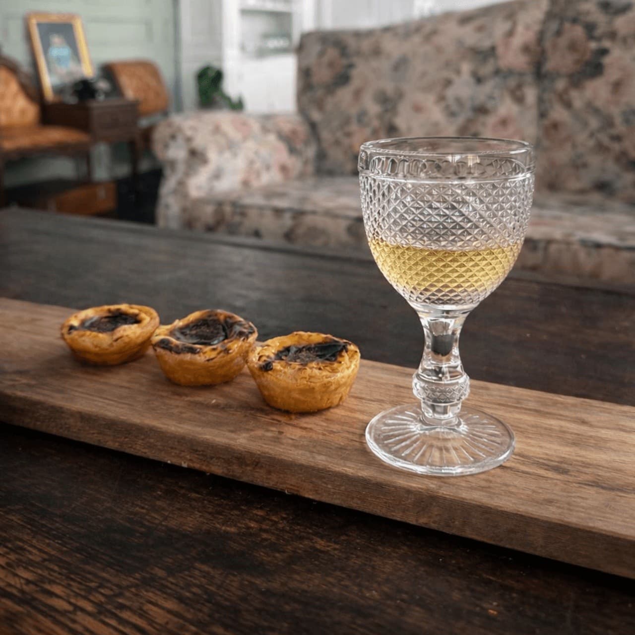 Wine glass next to custard tarts on wooden board