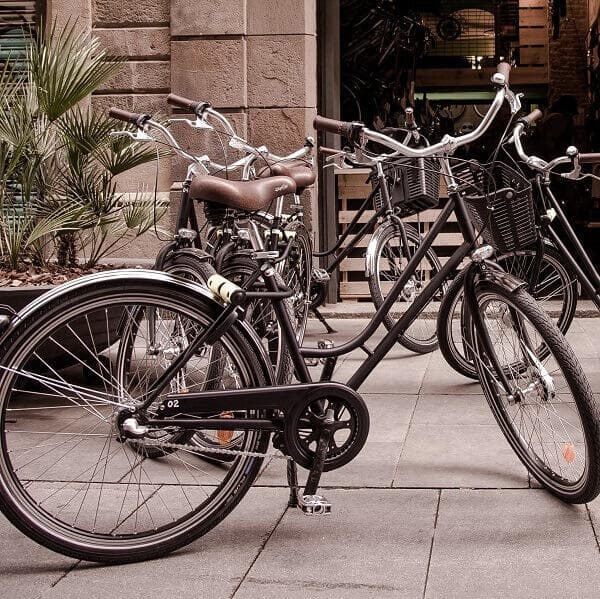 Multiple city bicycles parked on sidewalk outside shop, urban cycling.