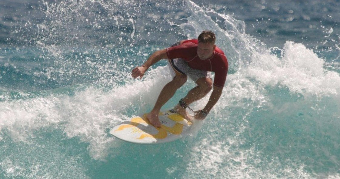 Surfer carving a wave on ocean reef near sunny coastline