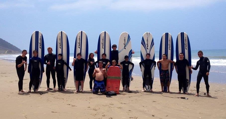 Surf class group posing with vertical boards on sandy beach