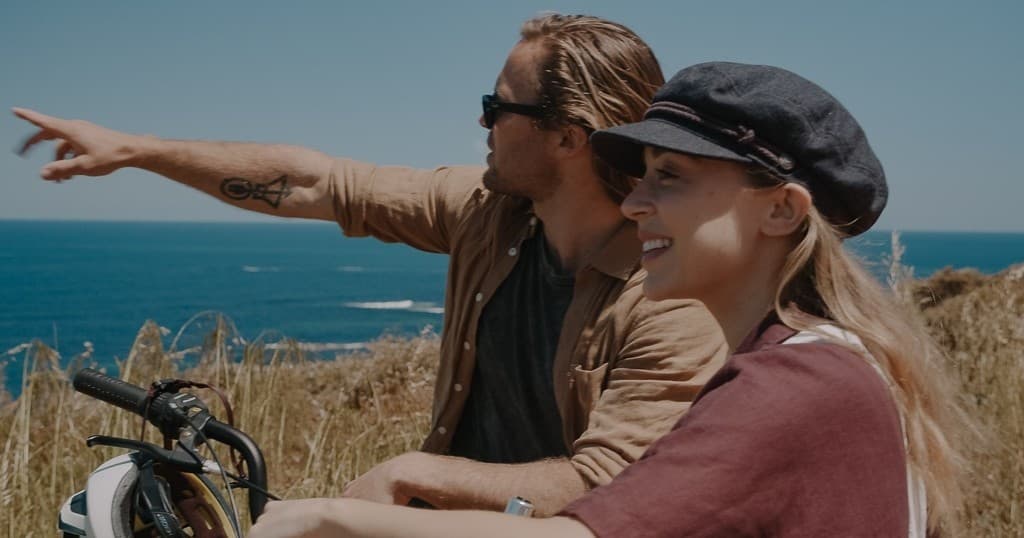 Couple pointing toward ocean while resting with bikes on bluff