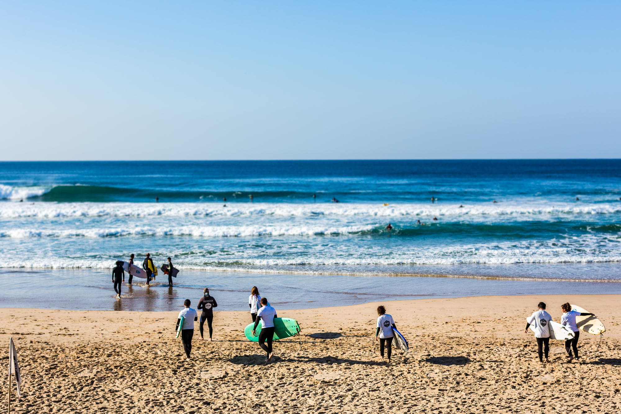 Group of surfers walking on sandy beach toward ocean waves