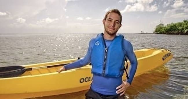 Solo kayaker standing by yellow kayak on calm coastal waters