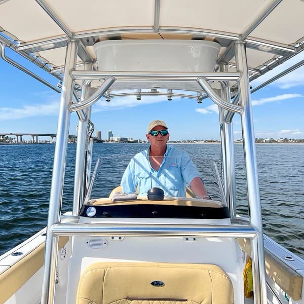 Captain steering center console boat under T-top on open water