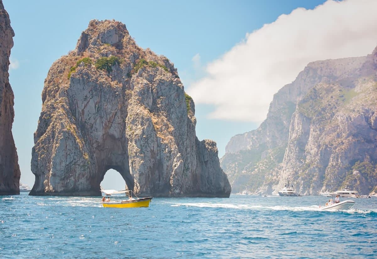 Boat passing Faraglioni sea arch near Capri for coastal cruising