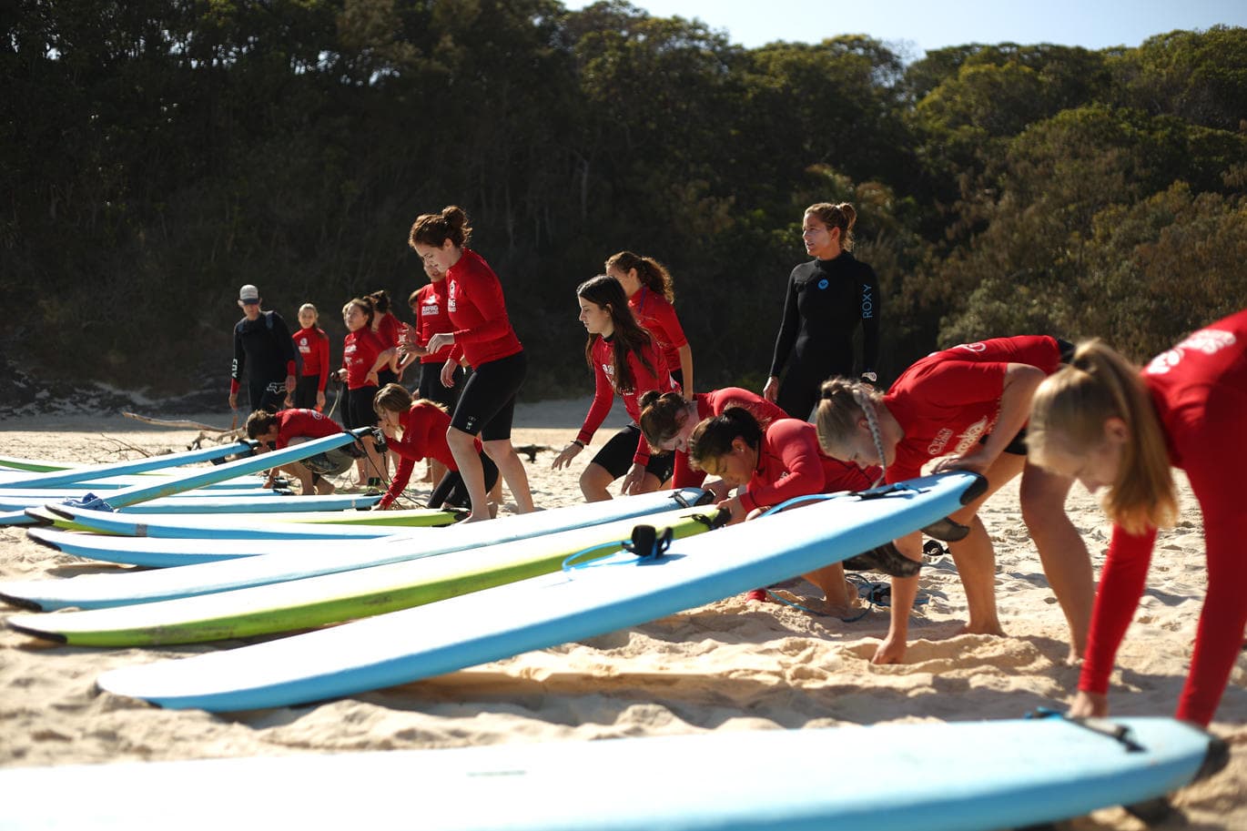 Surf school students practicing board drills on sandy beach