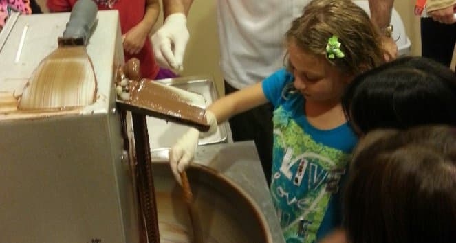 Child learning chocolate making on tempering machine during indoor tour
