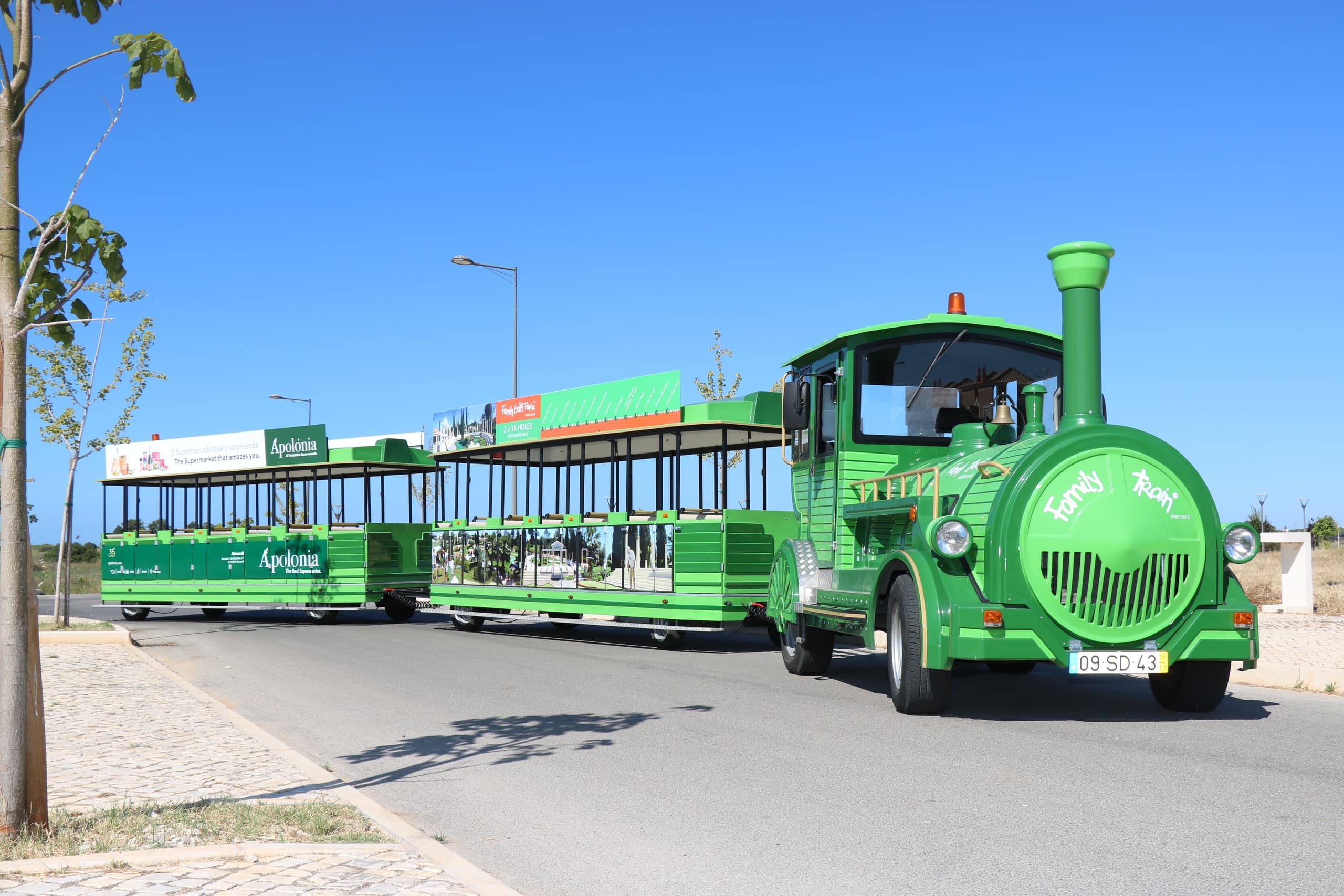 Green tourist road train parked by seaside road at family park