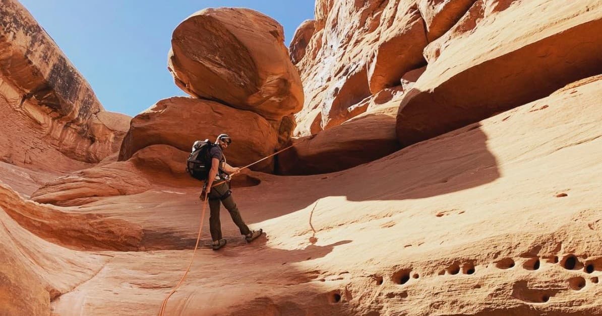 Hiker framed by sandstone arch overlooking vast desert canyon