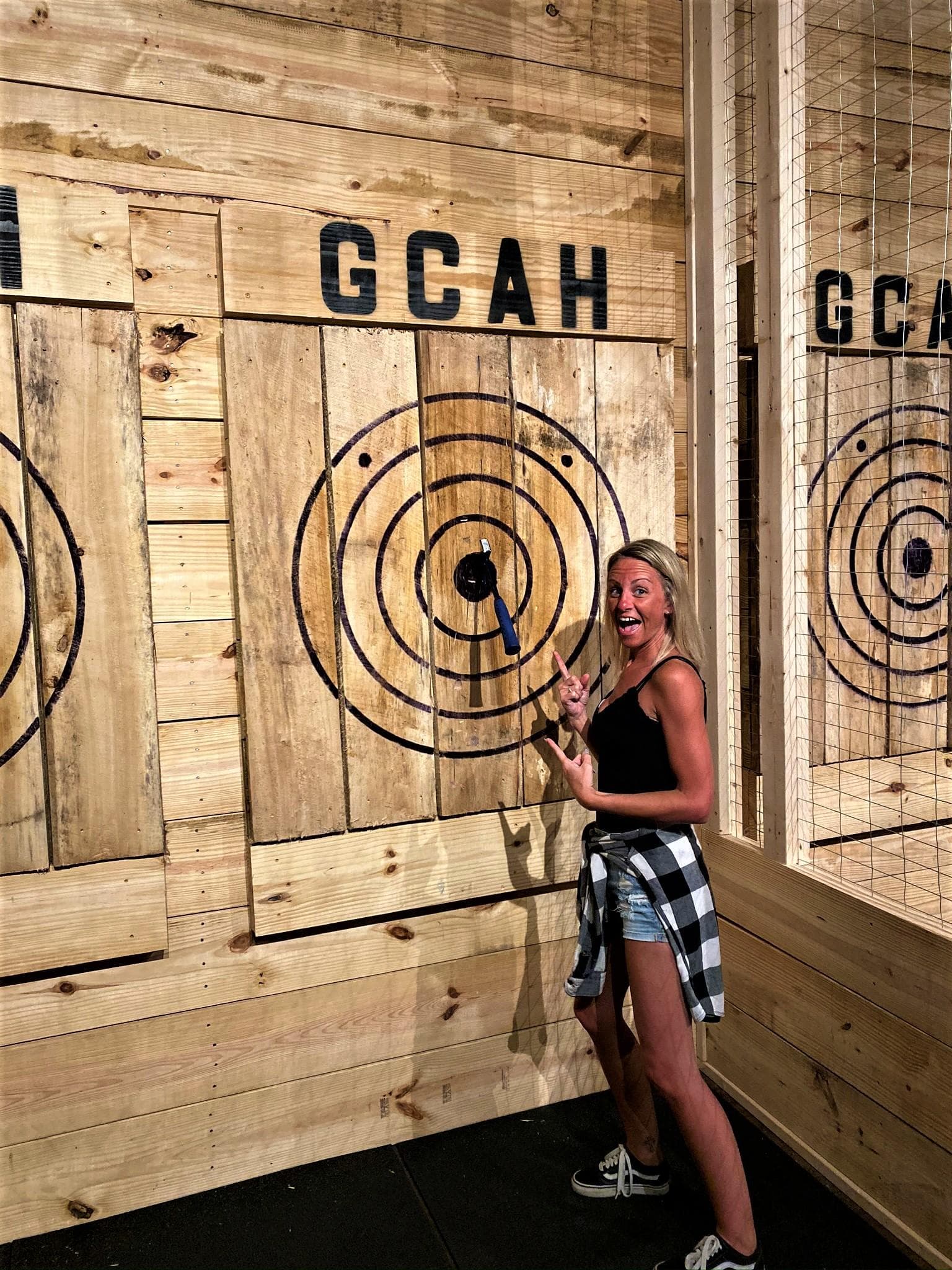 Woman posing at indoor axe-throwing wooden target in venue