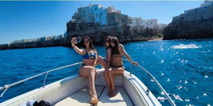 Boat tour with passengers posing off Polignano a Mare coastline