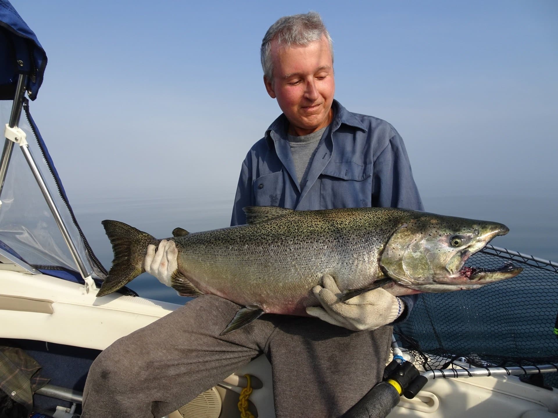 Fisherman seated on boat displaying trophy salmon over calm water