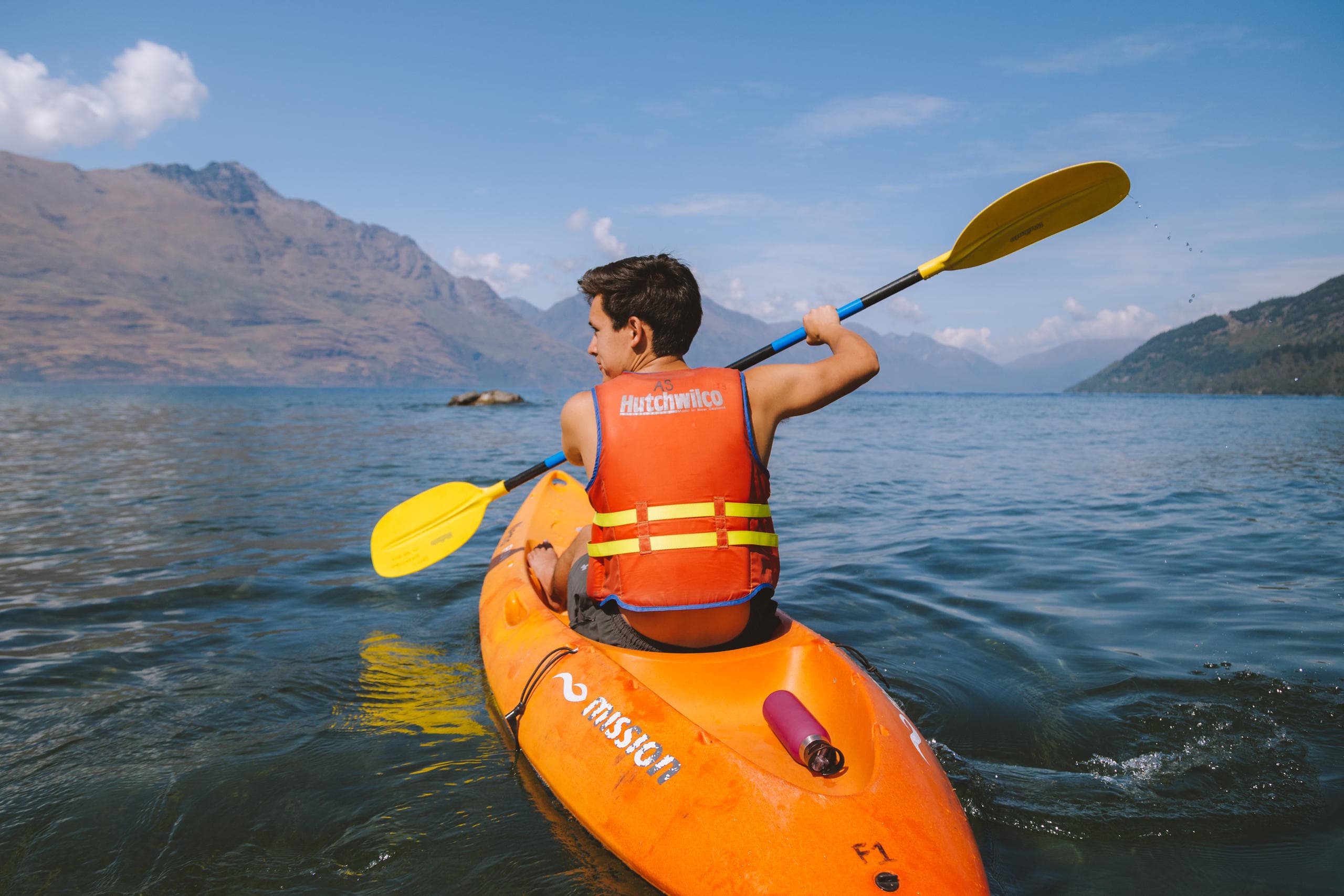 Solo kayaker paddling on alpine lake near rugged mountain shoreline