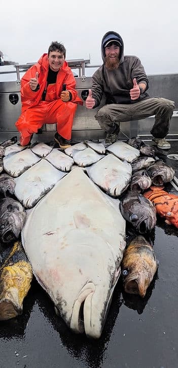 Crew posing with giant halibut and mixed catch on wet charter deck