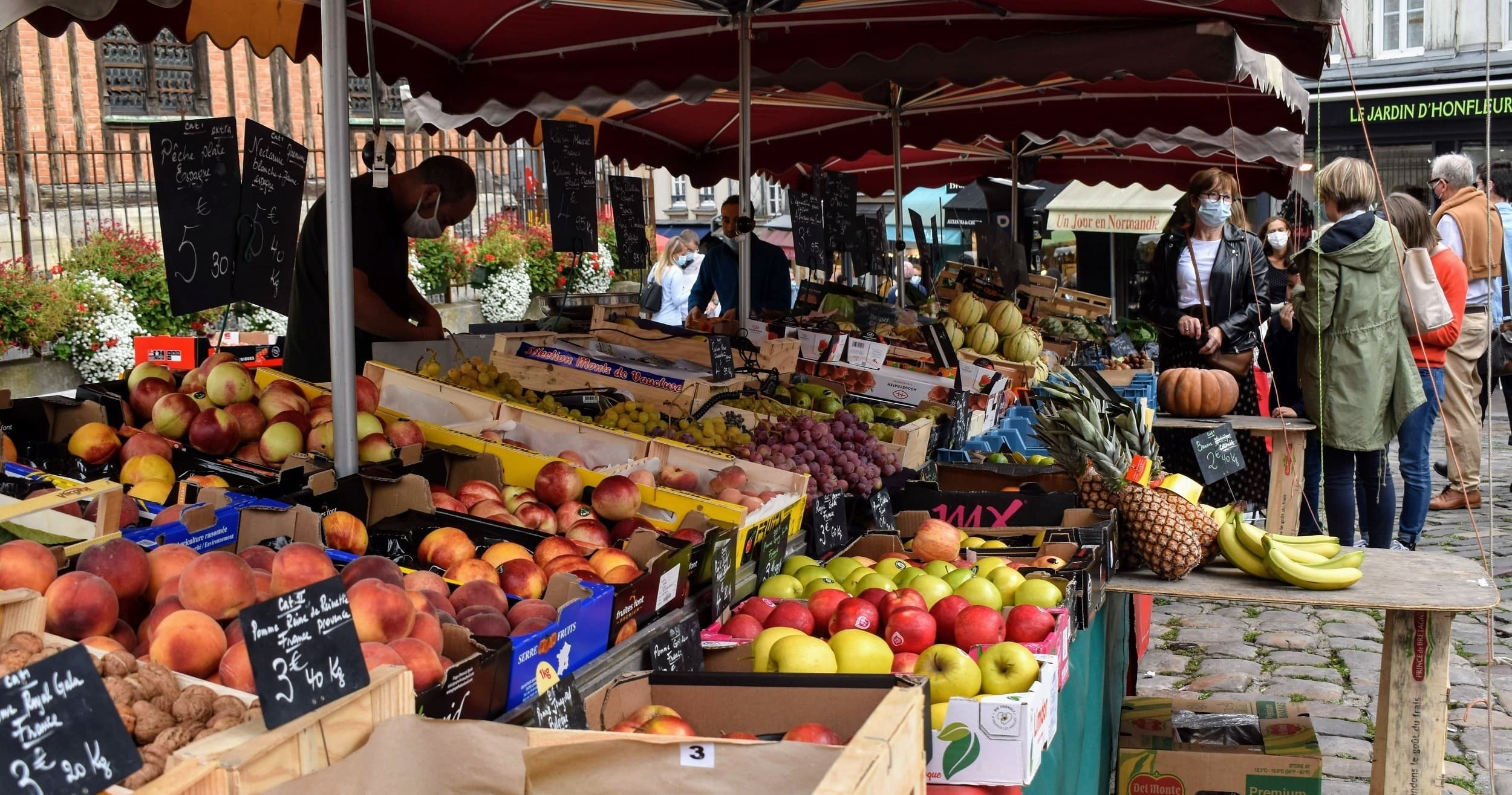 Outdoor produce market stalls in Honfleur with shoppers browsing