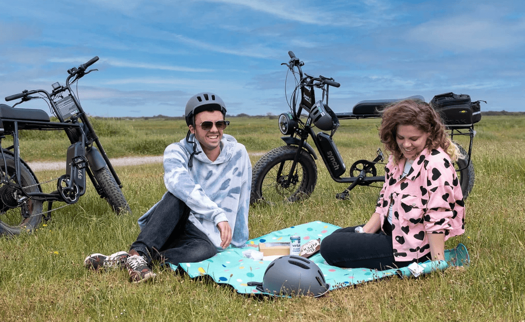 Couple picnicking beside e-bikes on grassy coastal marsh