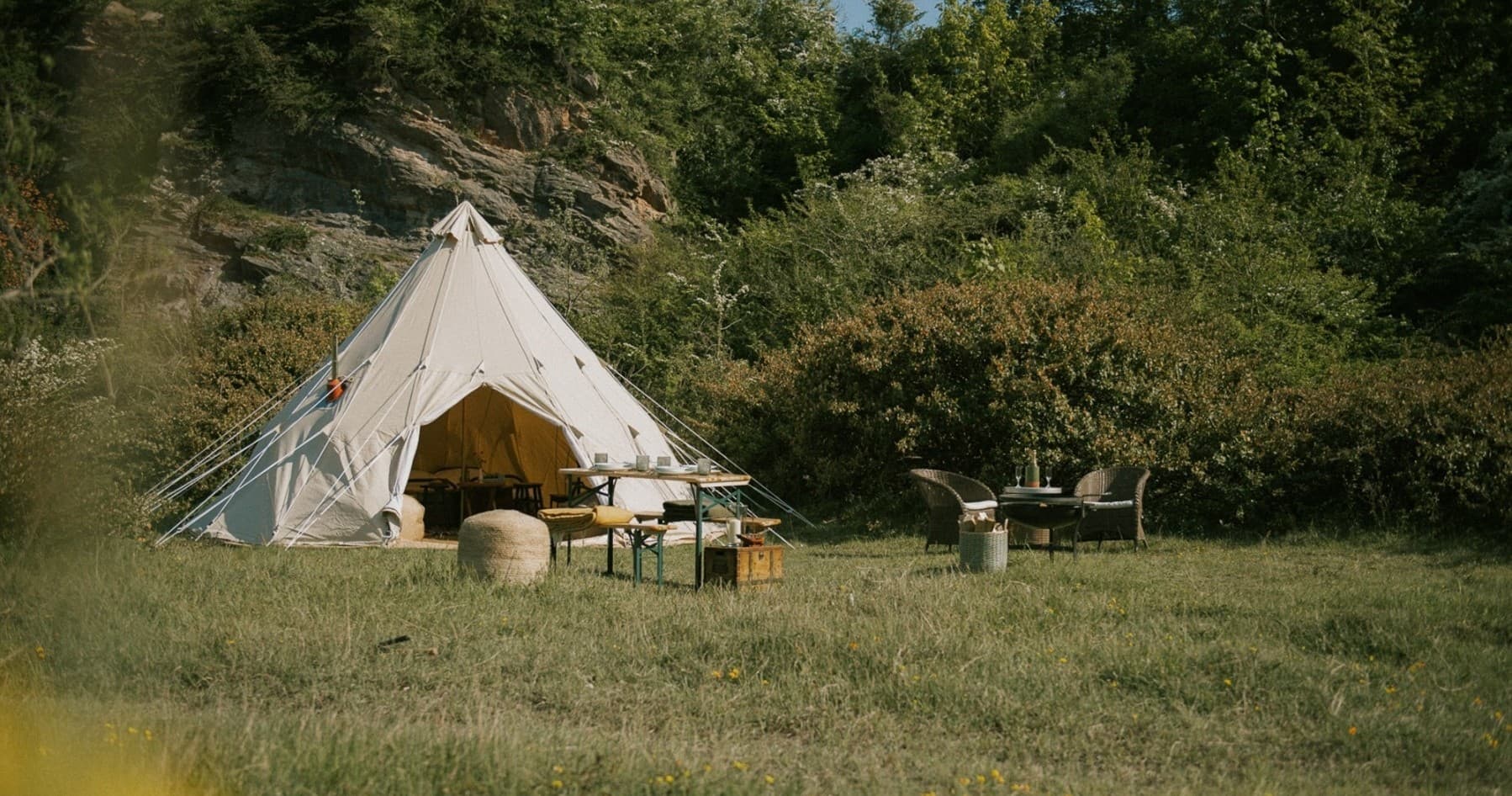 Canvas bell tent glamping in grassy meadow surrounded by trees