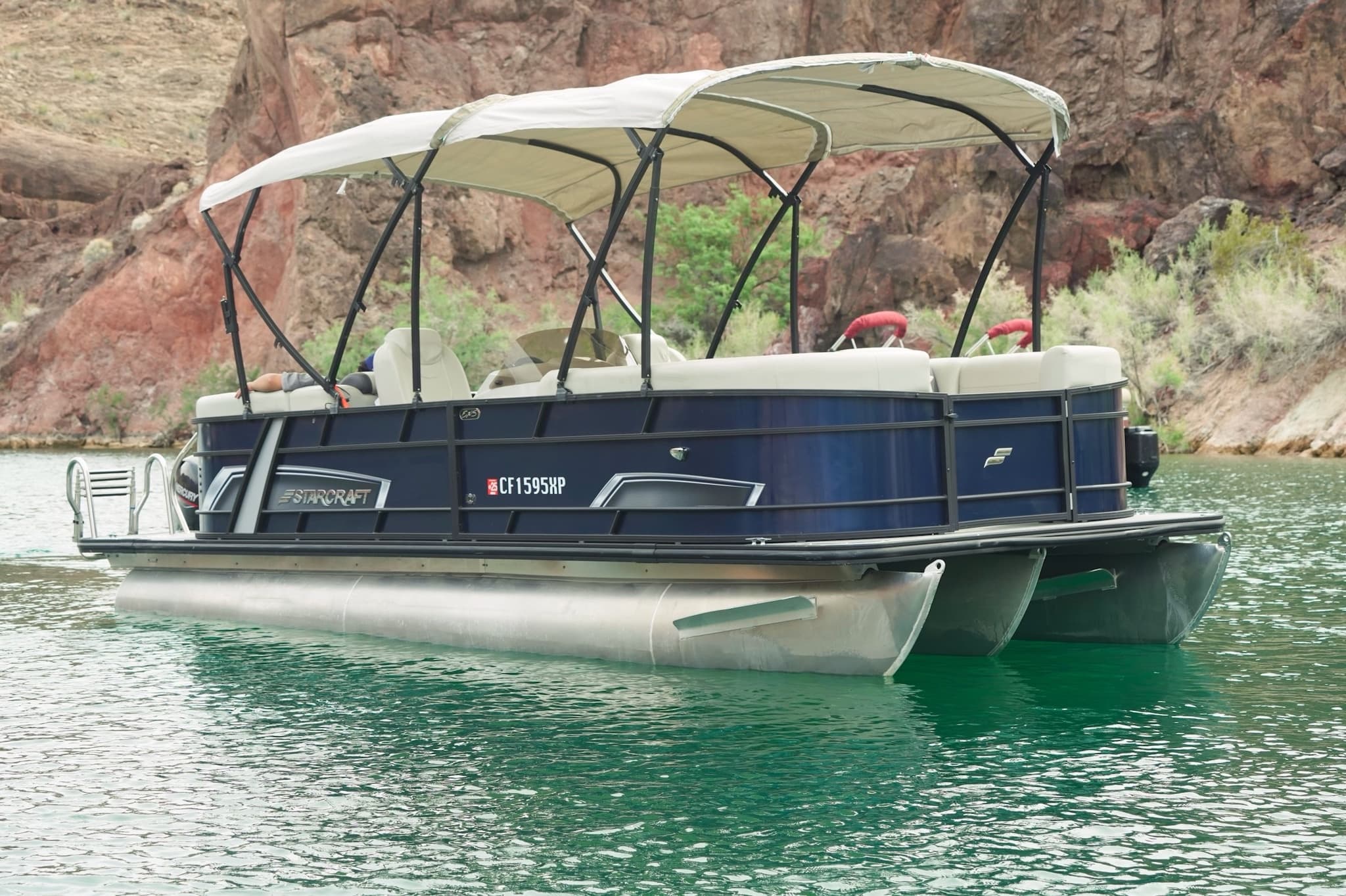 Pontoon boat anchored on calm lake by rocky shoreline and desert