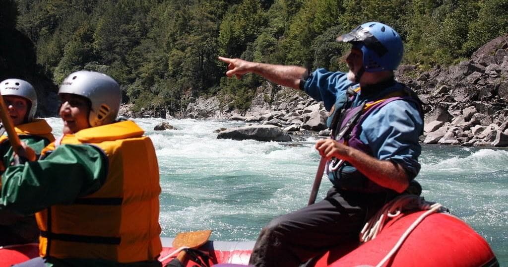 Guide steering inflatable raft down turquoise river through forested canyon