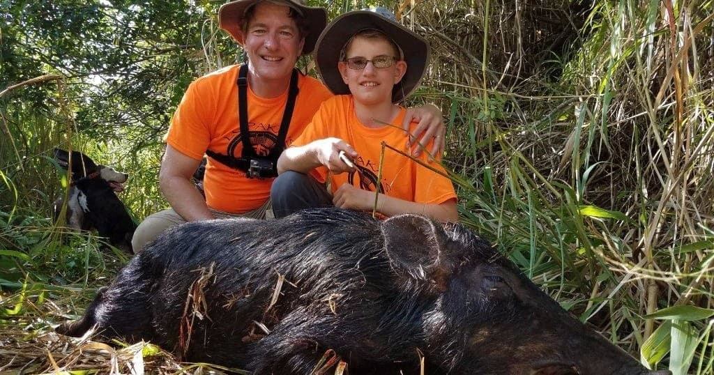 Parents and youth with wild boar in tall grass on guided hunt outing