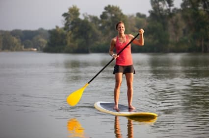 Stand-up paddleboarder paddling on peaceful tree-lined lake
