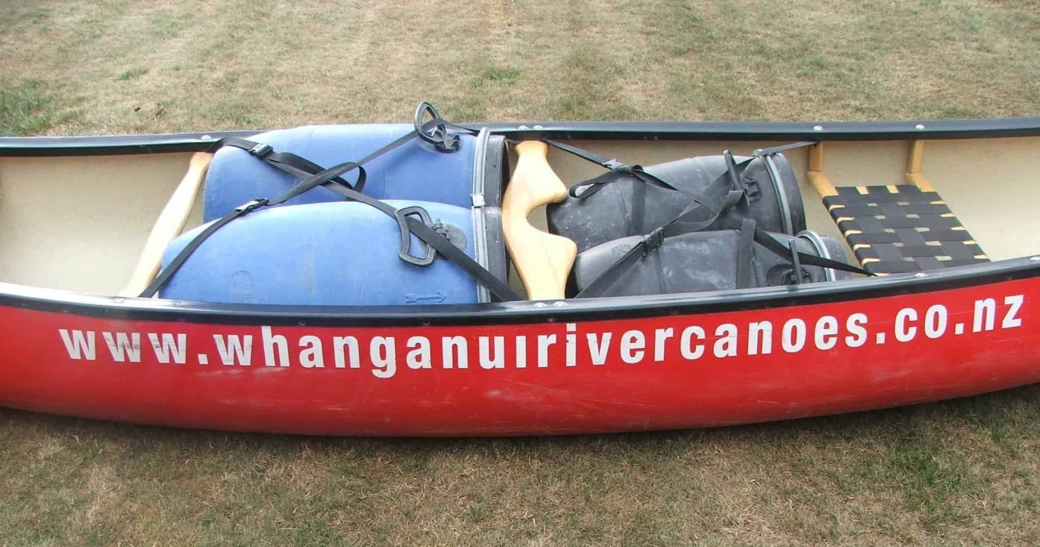 Red canoe with whanganui river canoes branding on riverbank NZ