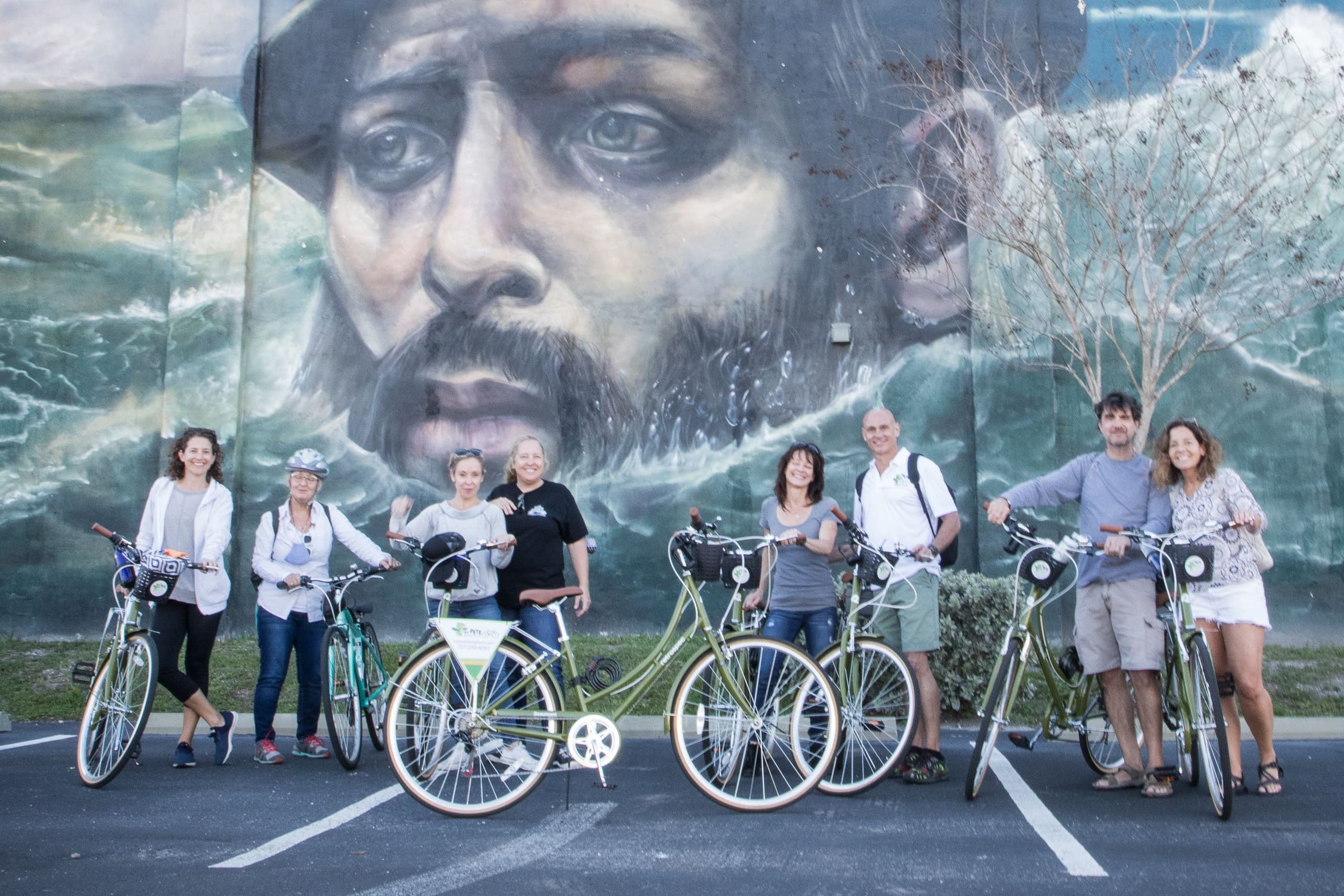 Friendly bike tour group posing by coastal mural in St. Pete