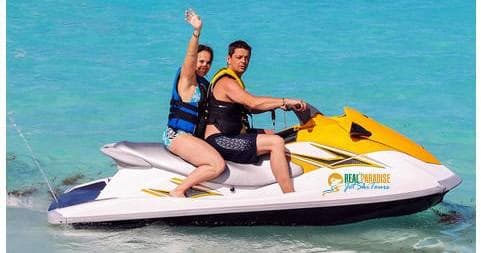 Couple riding jet ski on turquoise Caribbean waters, waving