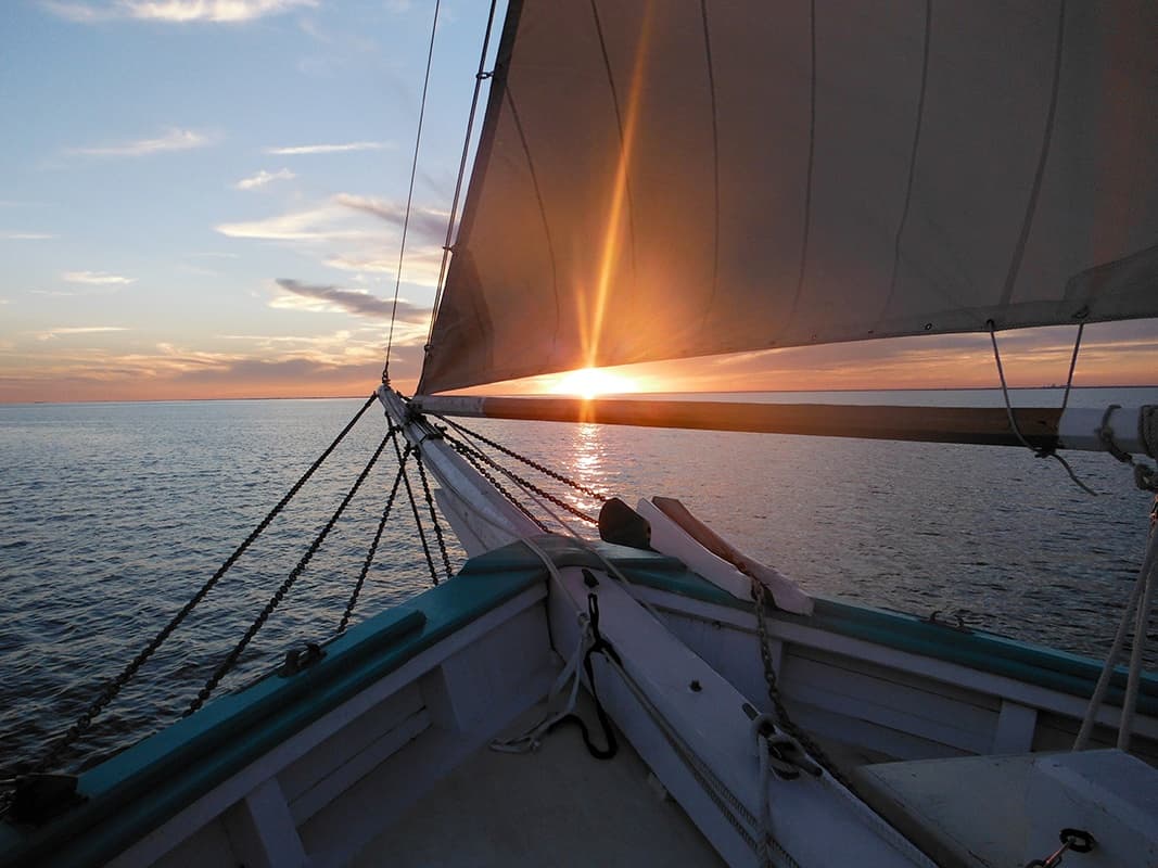 Sailboat bow at sunset with sunburst over open sea, Maine coast