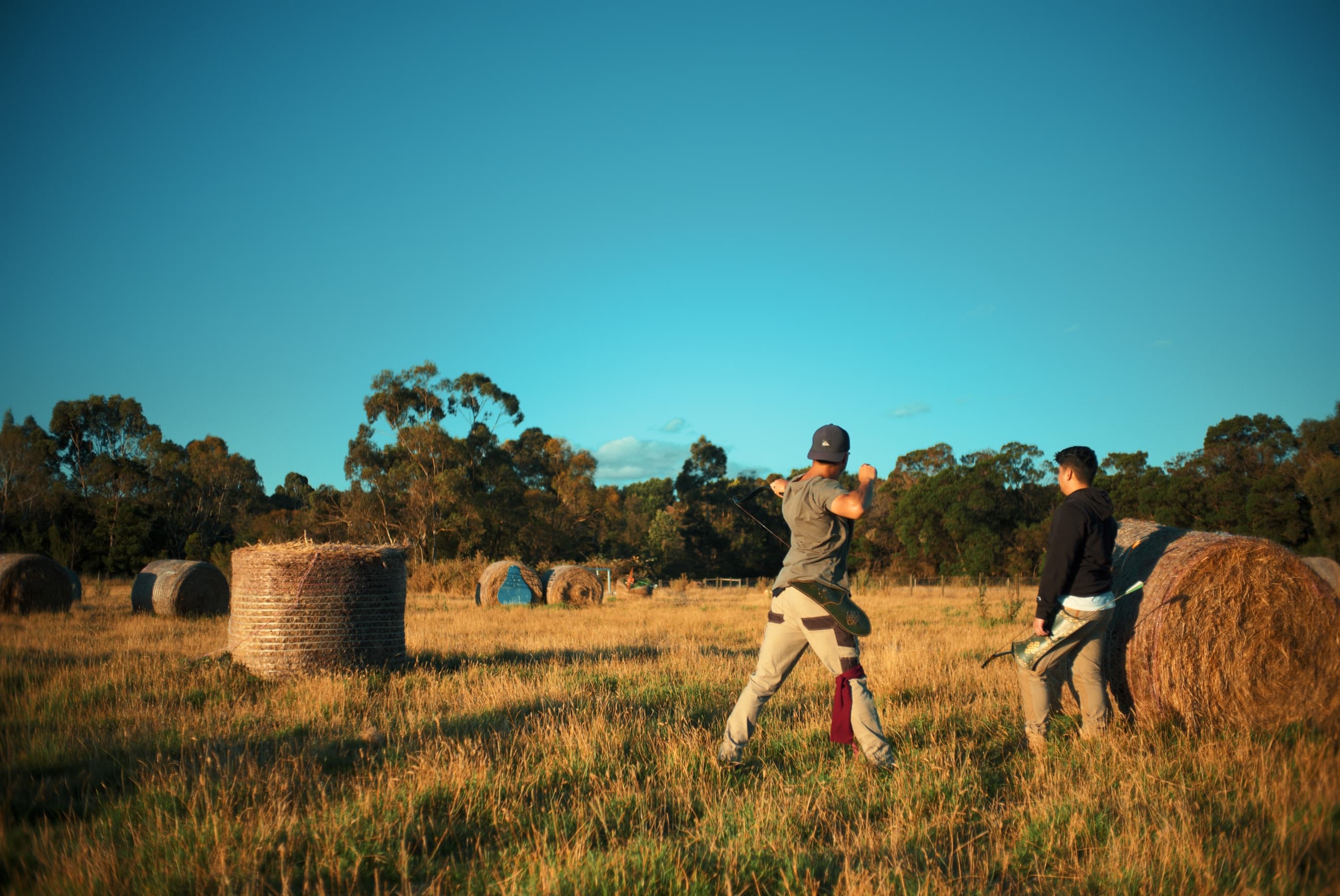 Archers practicing in golden hayfield at sunset, rural open field
