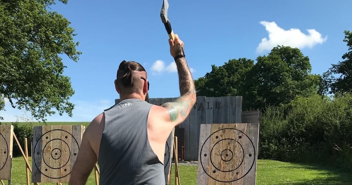 Axe thrower launching axe toward wooden targets in park