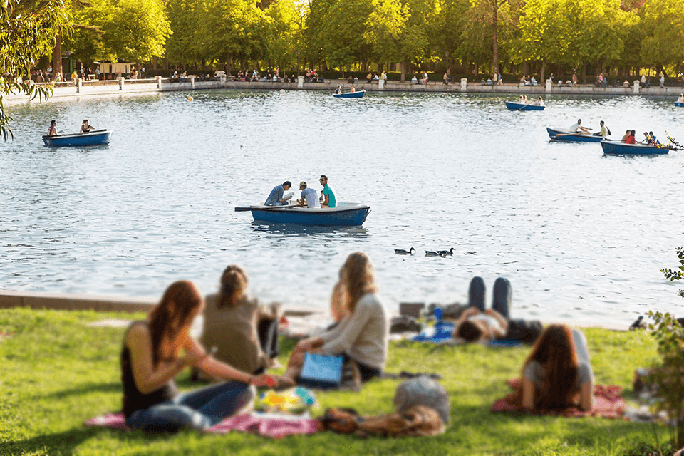 People picnicking by lake with paddle boats in Madrid park