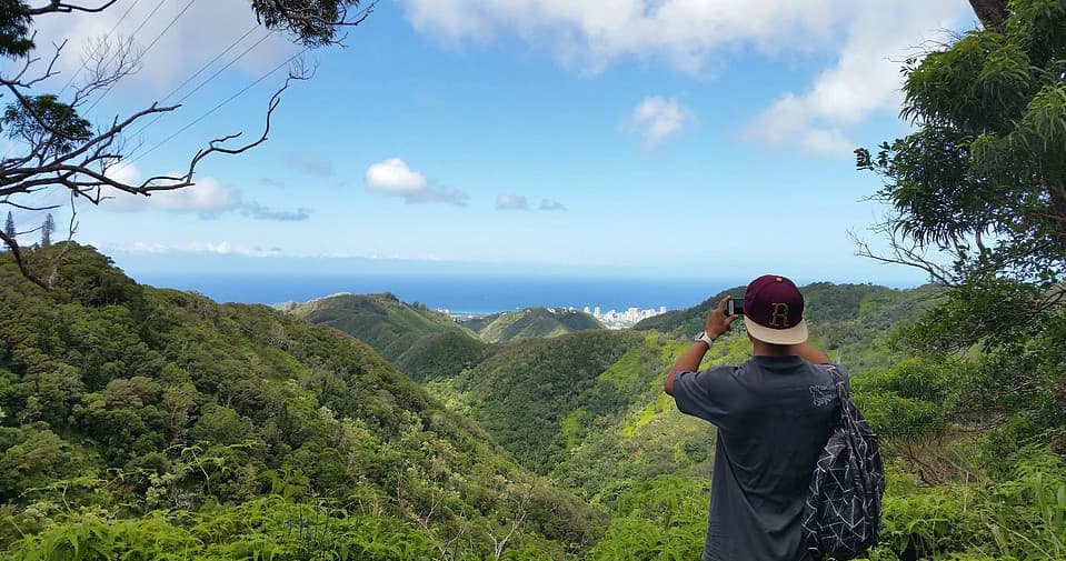 Hiker photographing lush Oahu mountain valley and ocean view