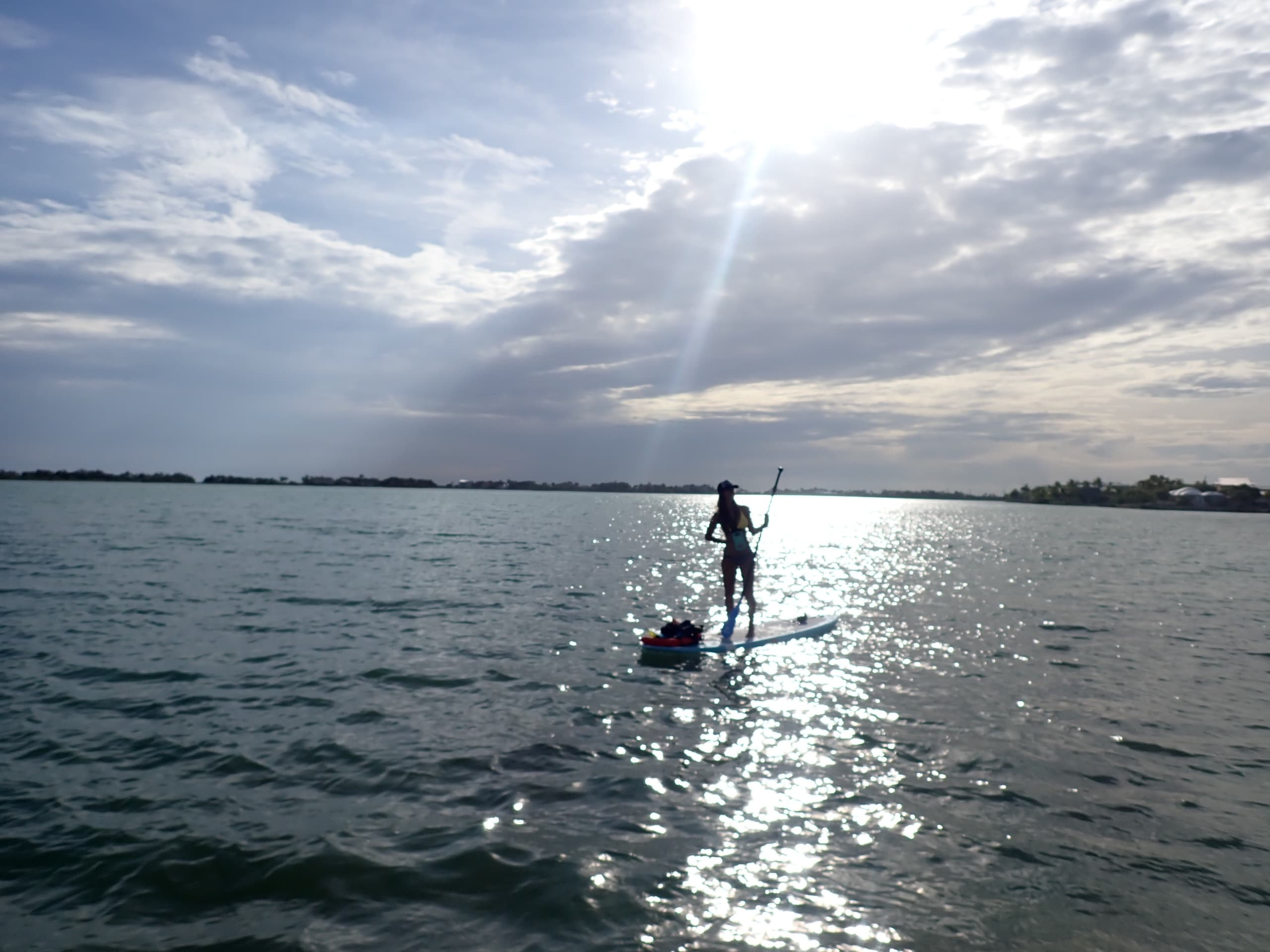 Stand-up paddleboarder gliding across reflective ocean at sunrise
