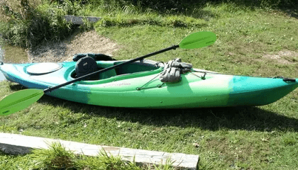 Single green kayak on grassy riverbank ready for paddling
