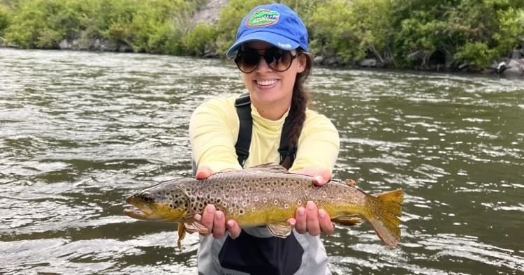 Smiling angler holding brown trout on Utah river, fly fishing