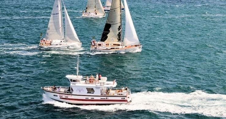Sailboats racing with motor support boat cutting through open ocean